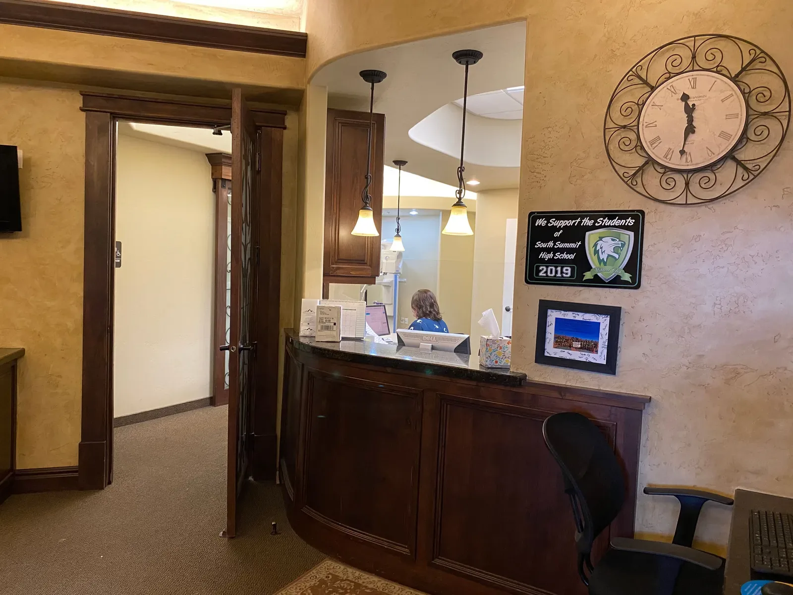 Reception desk with dark wood paneling, a decorative wall clock, and a staff member working behind the counter.